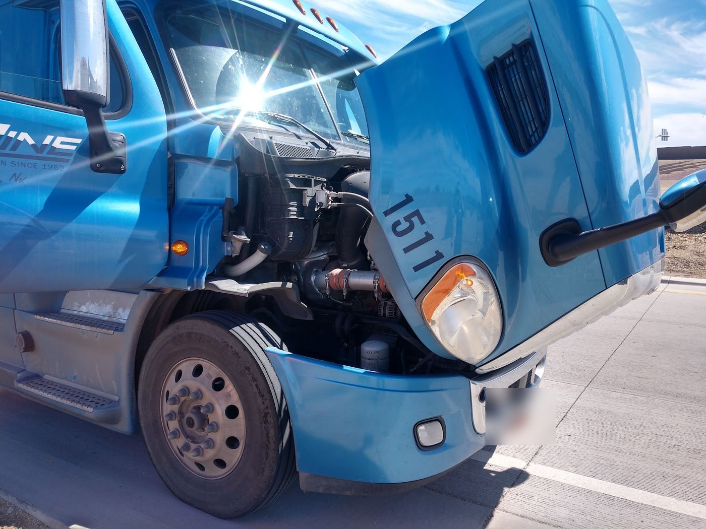 A blue semi truck with the hood tilted open for engine work