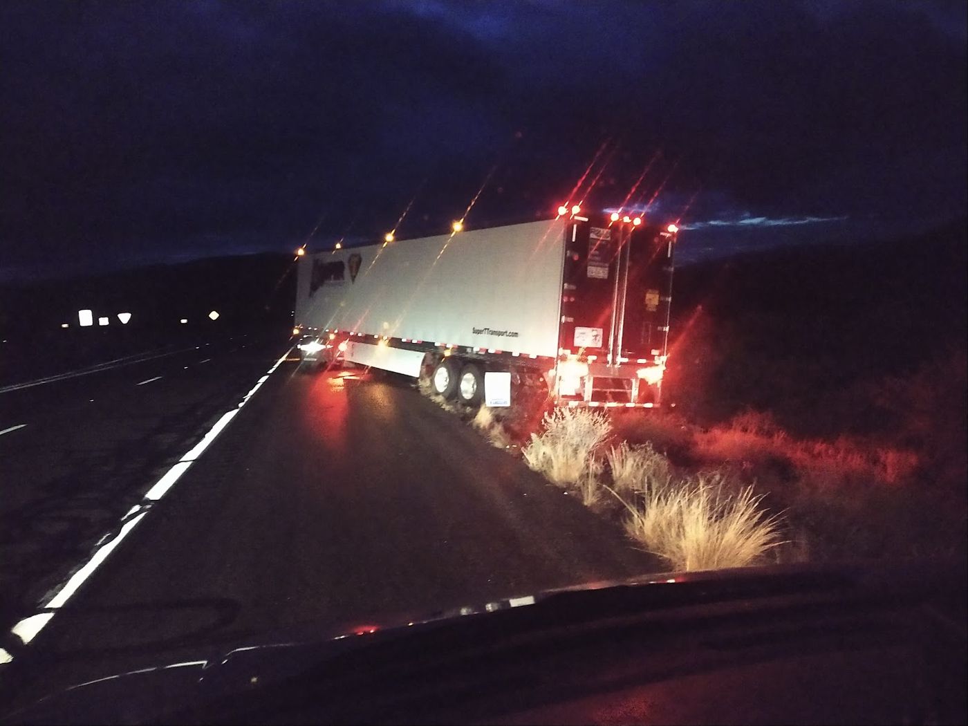 A semi trailer pulled off a dark highway at night with lights on